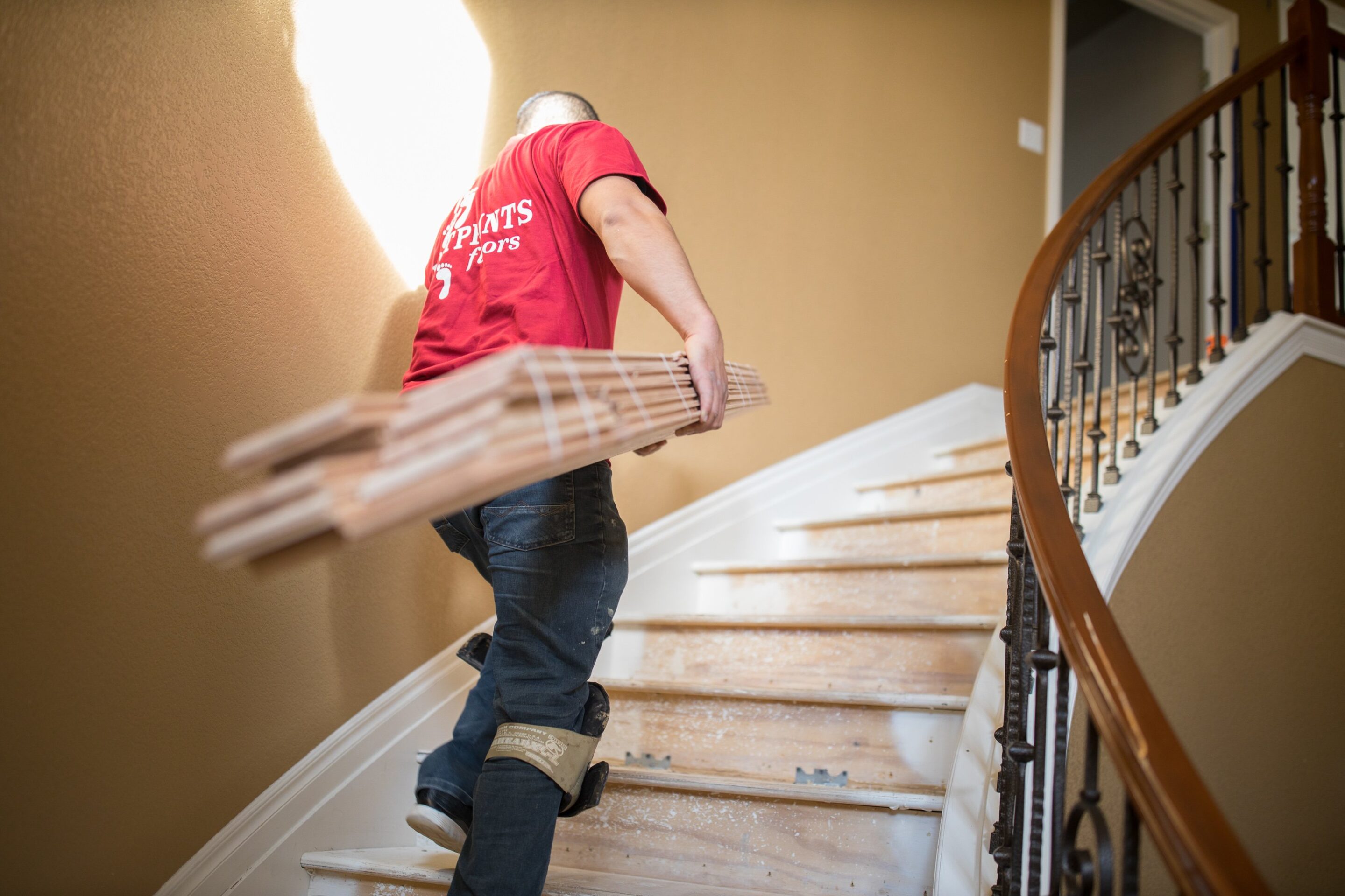 An image of a Footprints Floors team member carrying planks of flooring up stairs.