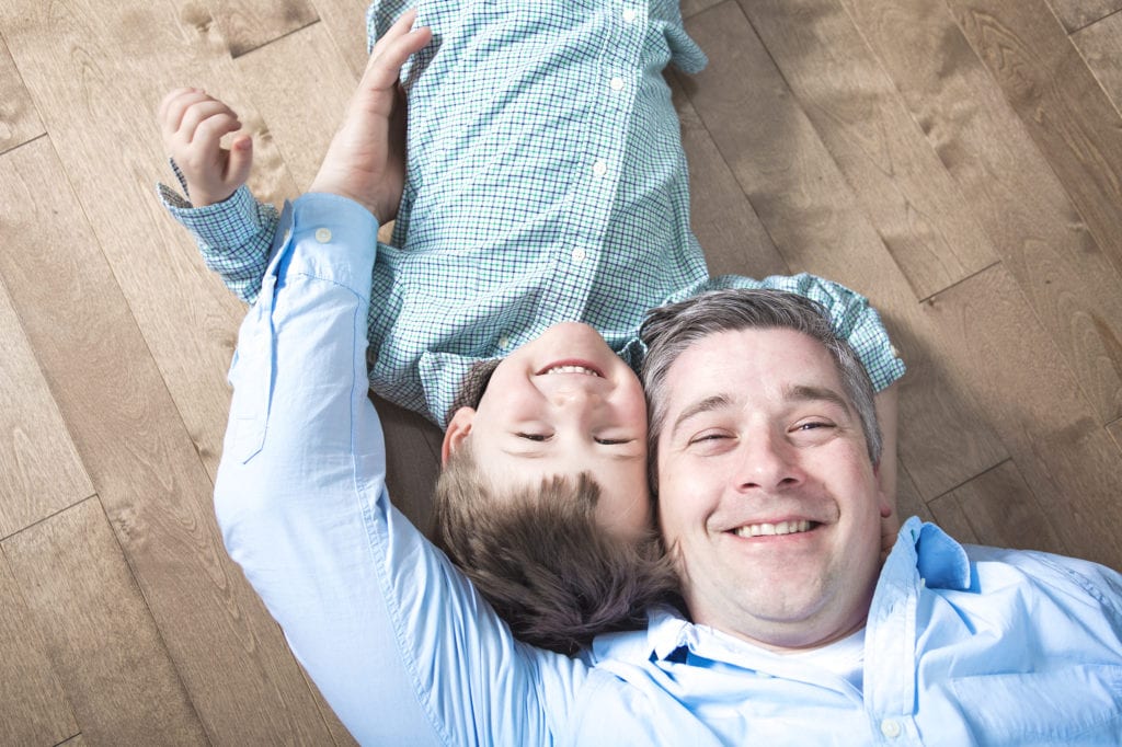 A father and son laying on newly installed hardwood floors - learn more about how to open a franchise to support your family.
