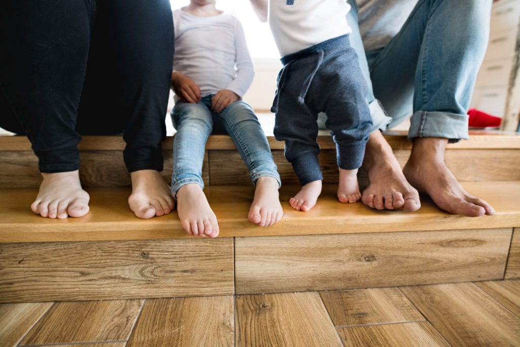 A family sitting on their hardwood floors on a staircase - contact Footprints Floors to learn how to open a franchise.