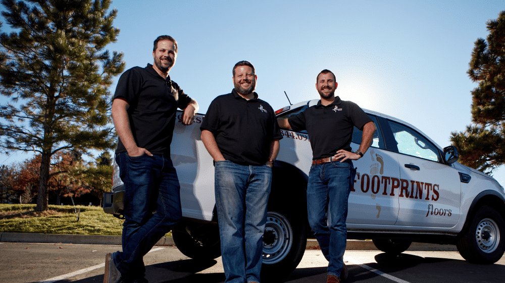 A large amount of Footprints Floors team members sitting and standing in front of a fleet of brand vans.