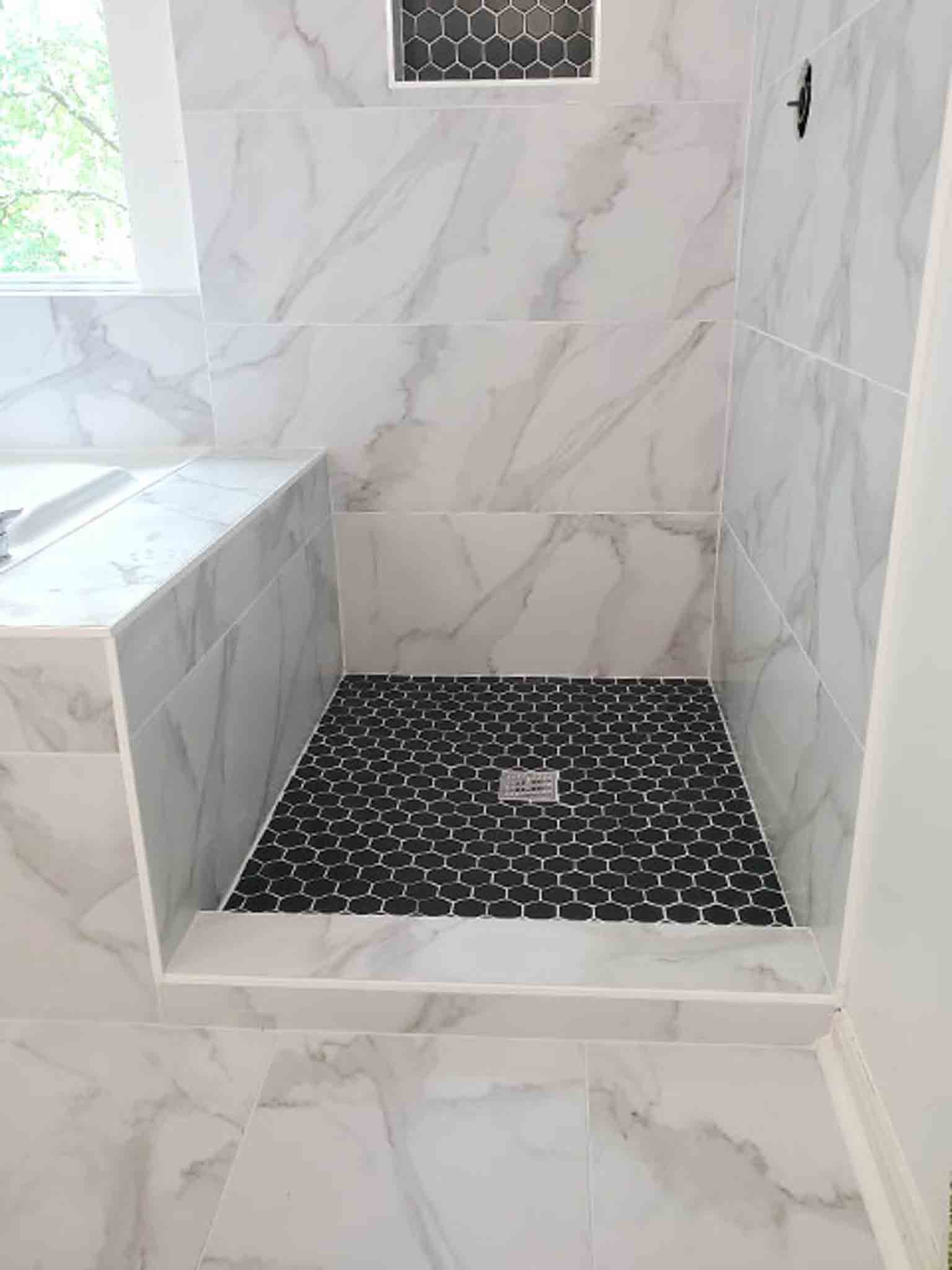 A white stand up shower with black tiling, installed Footprints Floors of the MidSouth.