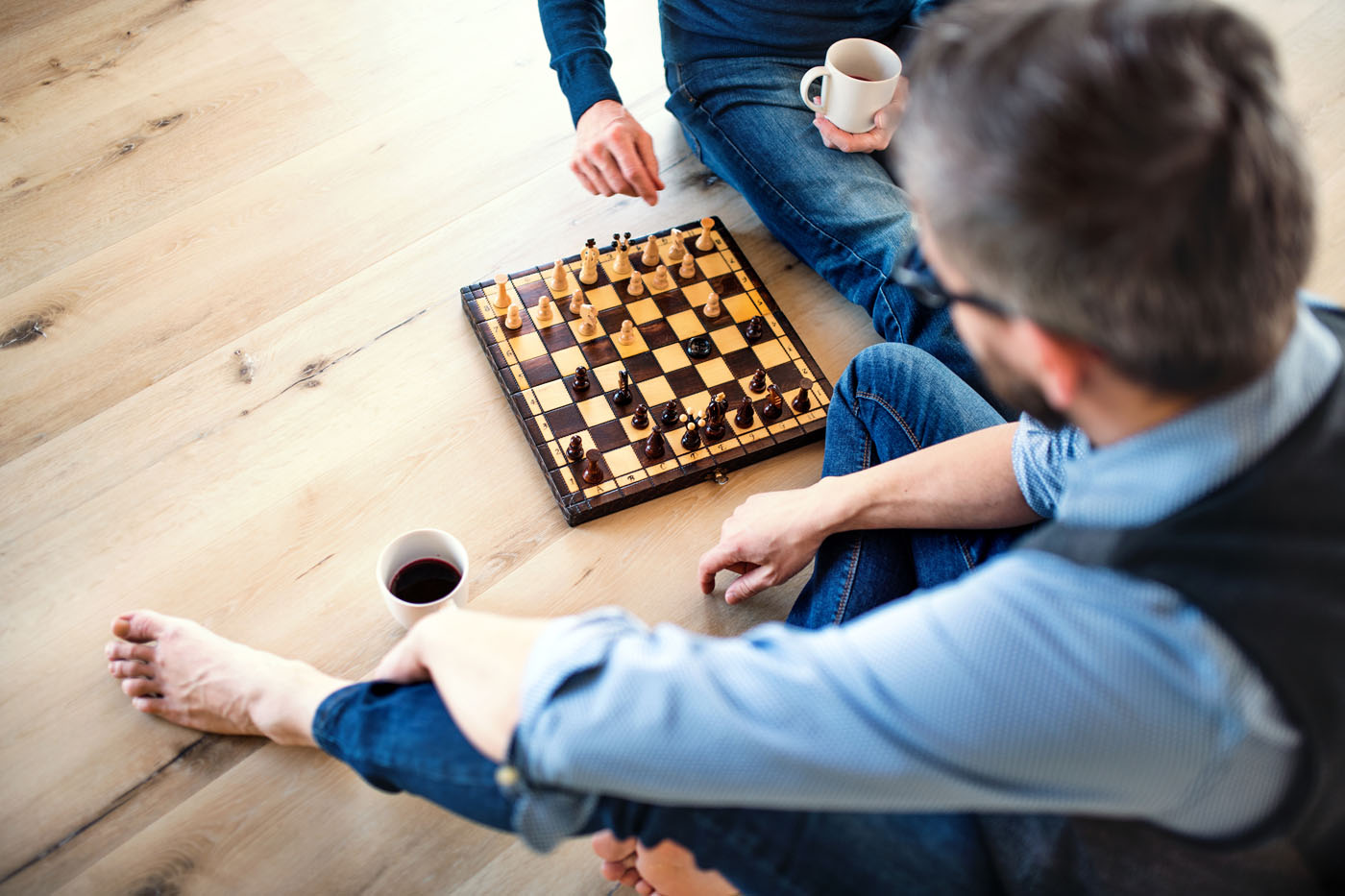 Two men sitting on an LVP floor playing chess.